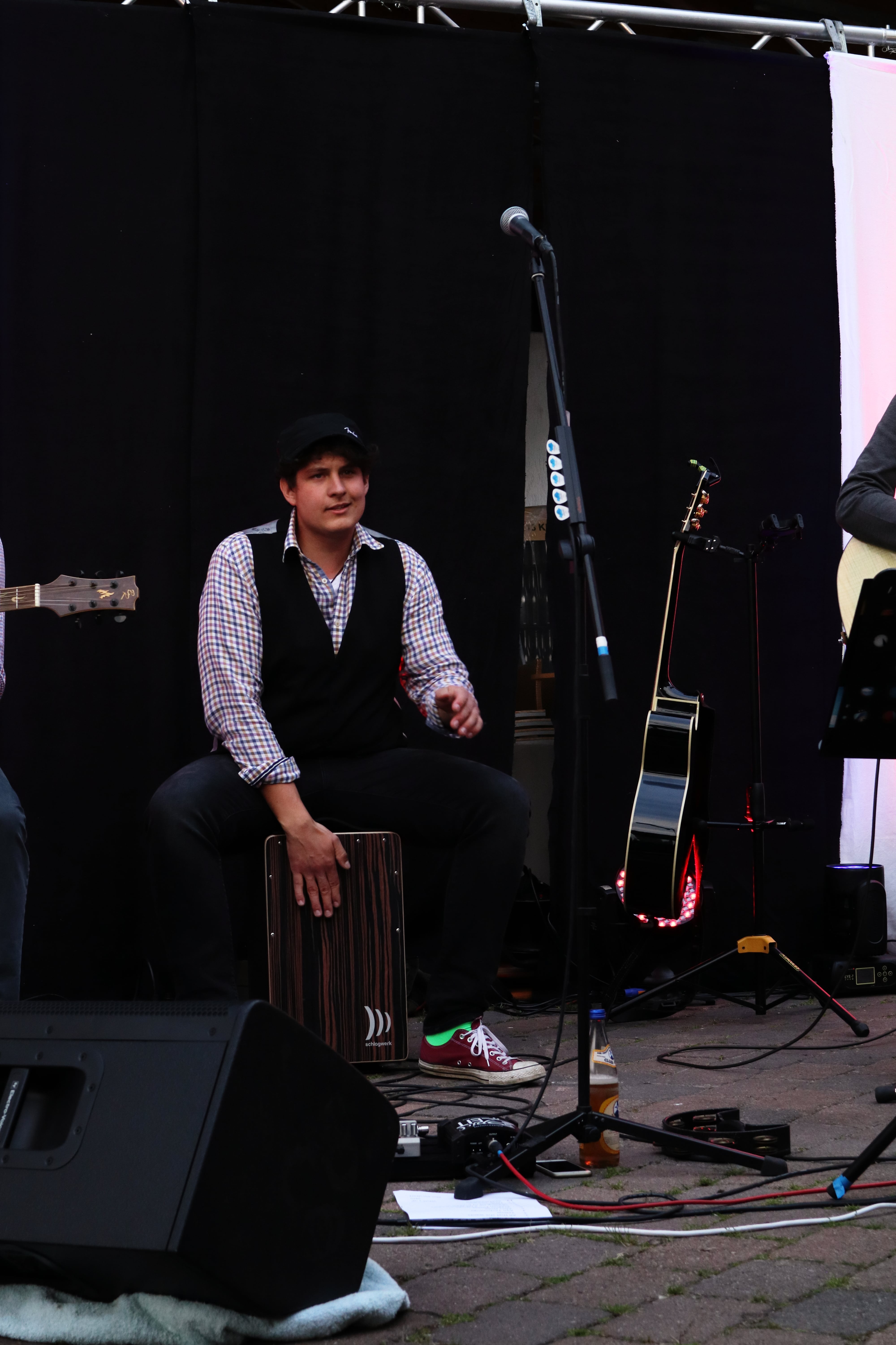 Auf dem Bild sieht man Tobi, wie er Cajon spielt. Im Hintergrund ist eine Gitarre zu sehen.